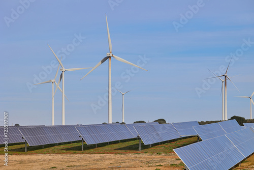 Solar panels and wind turbines under blue sky. Green energy concept.