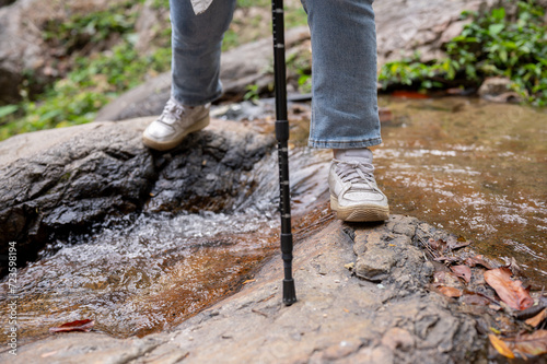 A female traveler with a trekking pole crossing water in a small canal while hiking on the mountain.