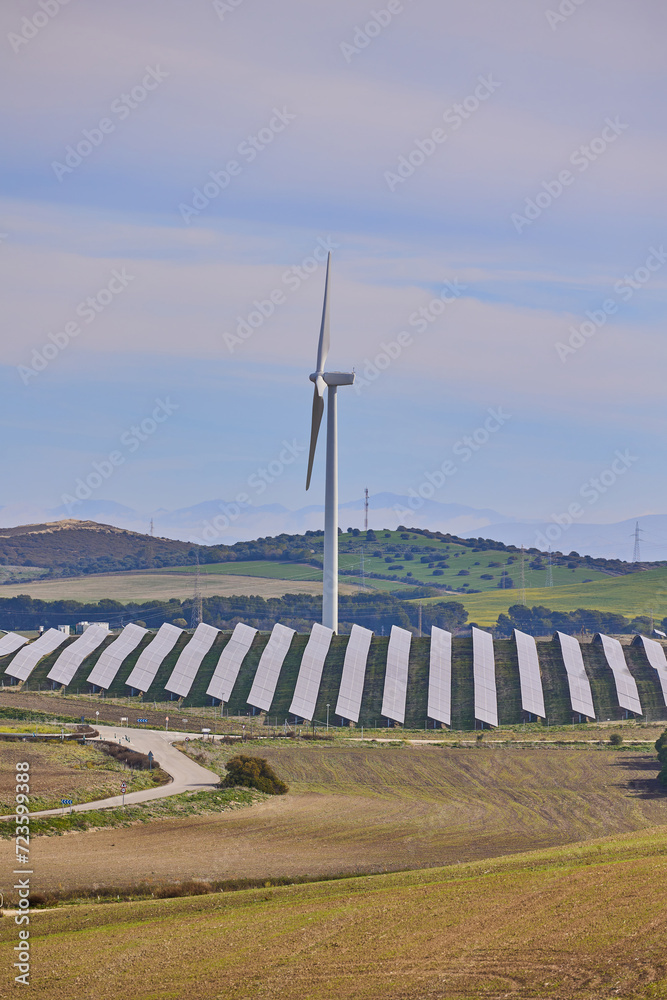 Solar panels and wind turbines with landscape of agricultural fields under blue sky. Green energy concept.