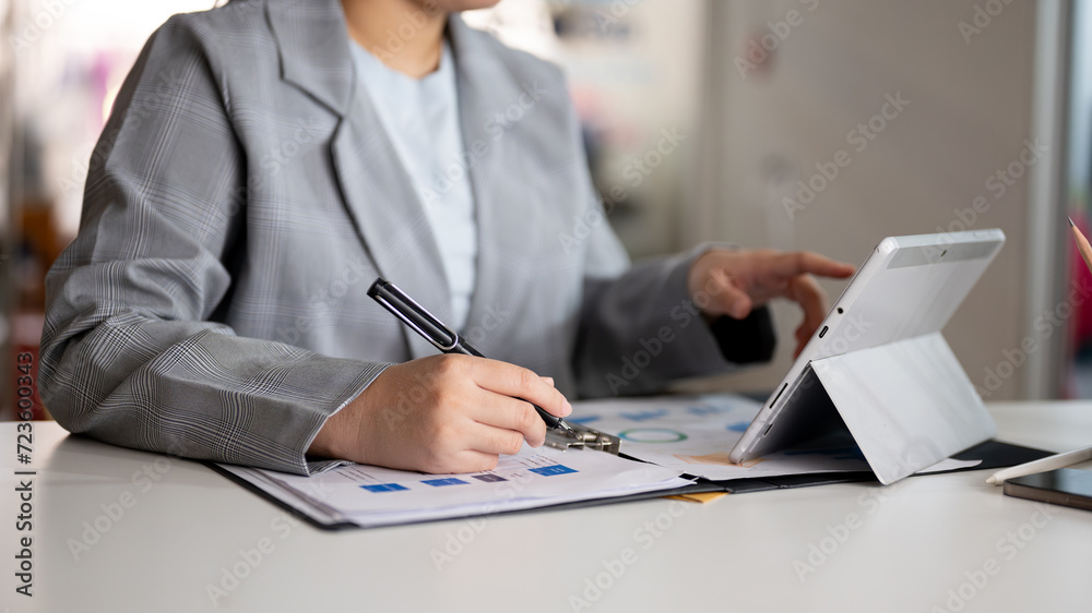 A businesswoman is working at her desk in the office, using her digital tablet and examining report. A businesswoman is working at her desk in the office, using her digital tablet and examining report.