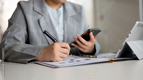 Cropped image of a businesswoman reading messages on her smartphone and taking notes on paperwork.