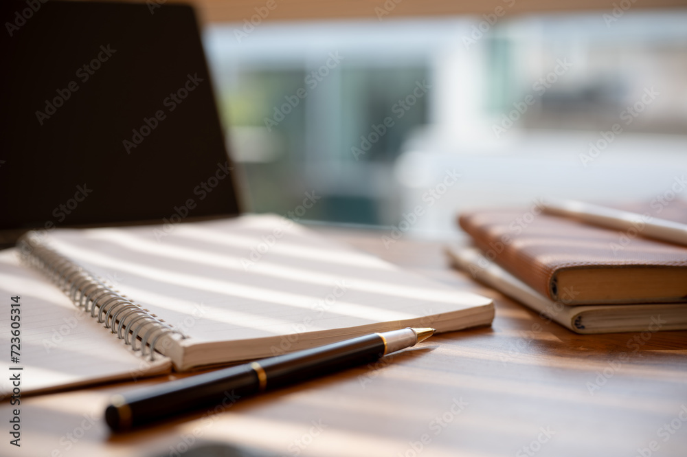 Close-up image of a wooden table with an opened book, a pen, books, and a laptop computer. Close-up image of a wooden table with an opened book, a pen, books, and a laptop computer.