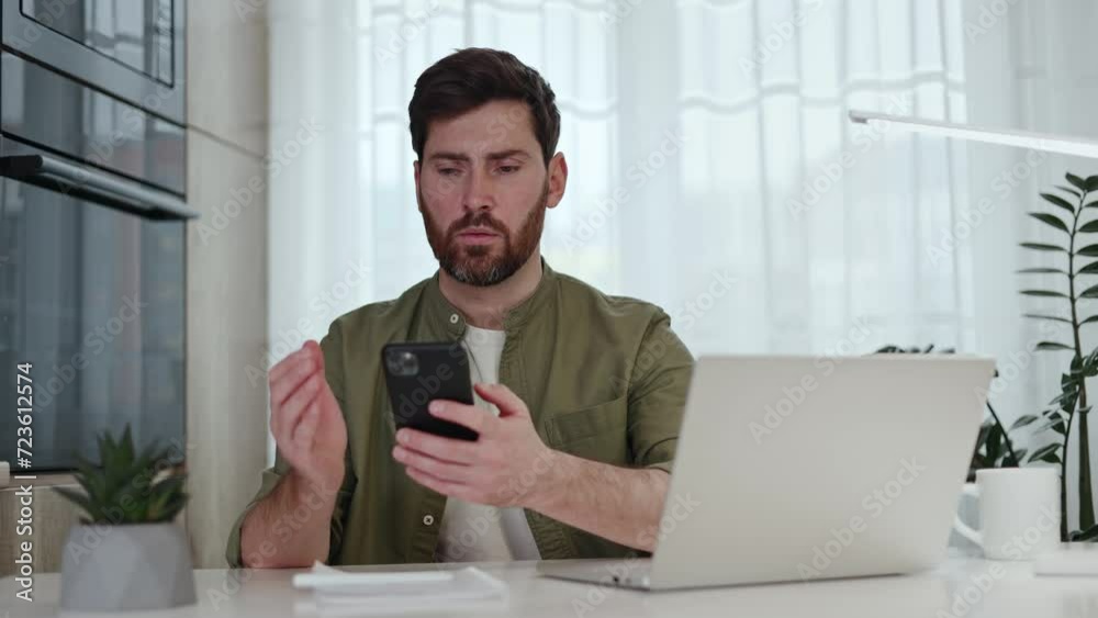 Upset male worker feeling disappointed by poor performance of personal smartphone in home office. Perplexed caucasian freelancer dressed in casual green shirt trying to surf internet on modern gadget. Upset male worker feeling disappointed by poor performance of personal smartphone in home office. Perplexed caucasian freelancer dressed in casual green shirt trying to surf internet on modern gadget.