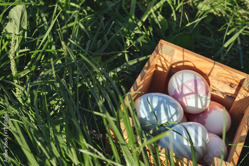 Multicolored eggs lie in a wooden box on the grass in the garden on a sunny spring day. Easter religious holiday concept. Copy space
