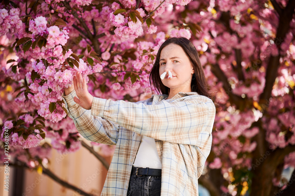 Woman allergic suffering from seasonal allergy and runny nose disease at spring. Young woman with paper tissues inserted into nose - symbolic gesture of inability to breathe due to nasal congestion. Woman allergic suffering from seasonal allergy and runny nose disease at spring. Young woman with paper tissues inserted into nose - symbolic gesture of inability to breathe due to nasal congestion.