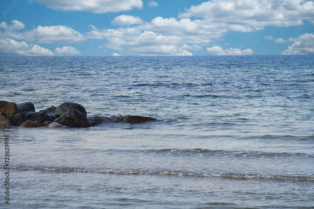 Fototapeta premium By the sea of the Baltic Sea. Stone groynes reach into the blue water. White clouds in the sky. Landscape shot of the coast.