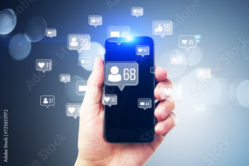 Close up of businessman hands holding smartphone with creative social media icons hologram on blurry background. Community, likes, shares and communication concept.