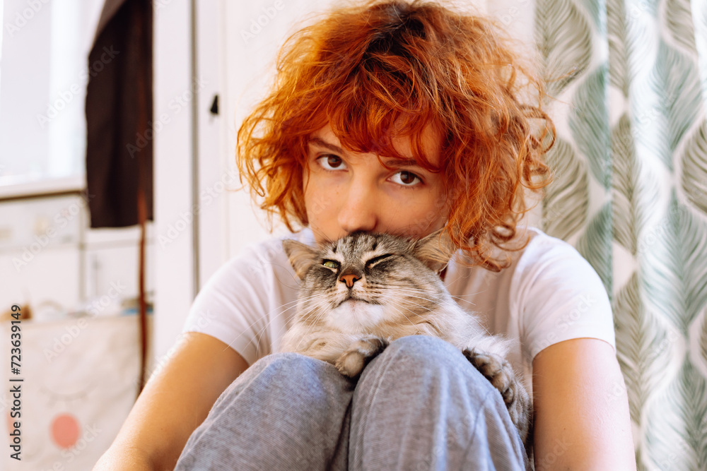 Fototapeta premium Portrait red-haired curly teenage girl with favorite fluffy domestic cat
