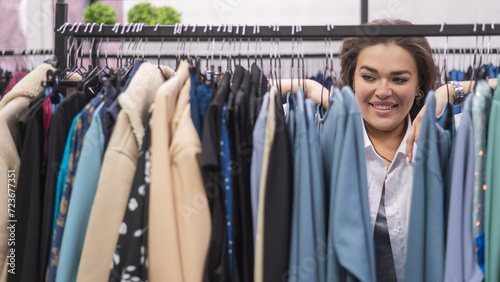 A smiling fat woman in a plus size store chooses clothes while sorting through the hangers. 
