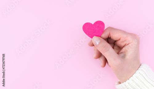 Woman's hand holds a pink heart on a pink background. Banner. Copy space. Top view. Selective focus.