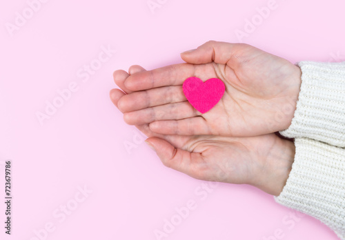 Pink heart in woman's hands on a pink background. Banner. Copy space. Top view. Selective focus.