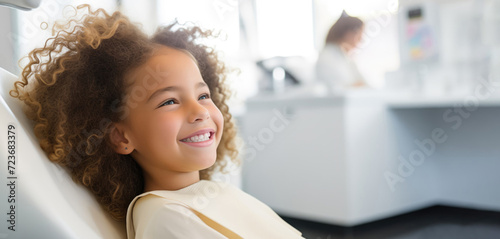Banner with little black girl in dentist chair, looks happy with treatment, on blurred background with space for text. Children's dentistry, routine checkup, no fear of treatment and pain