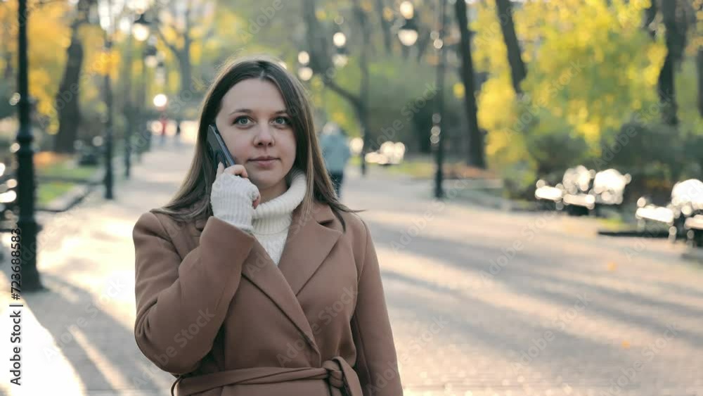 Woman on Phone in Autumn Park, Young woman in a brown coat talking on the phone, autumn trees in the background, city park scene Woman on Phone in Autumn Park, Young woman in a brown coat talking on the phone, autumn trees in the background, city park scene