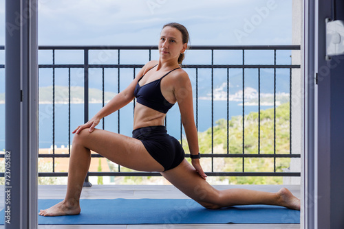 Yogi woman in sportswear stretching legs on the mat at the balcony