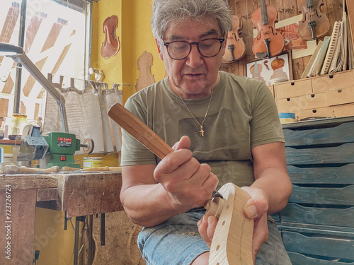 Fotografie master luthier violin maker working on violin scroll in his workshop