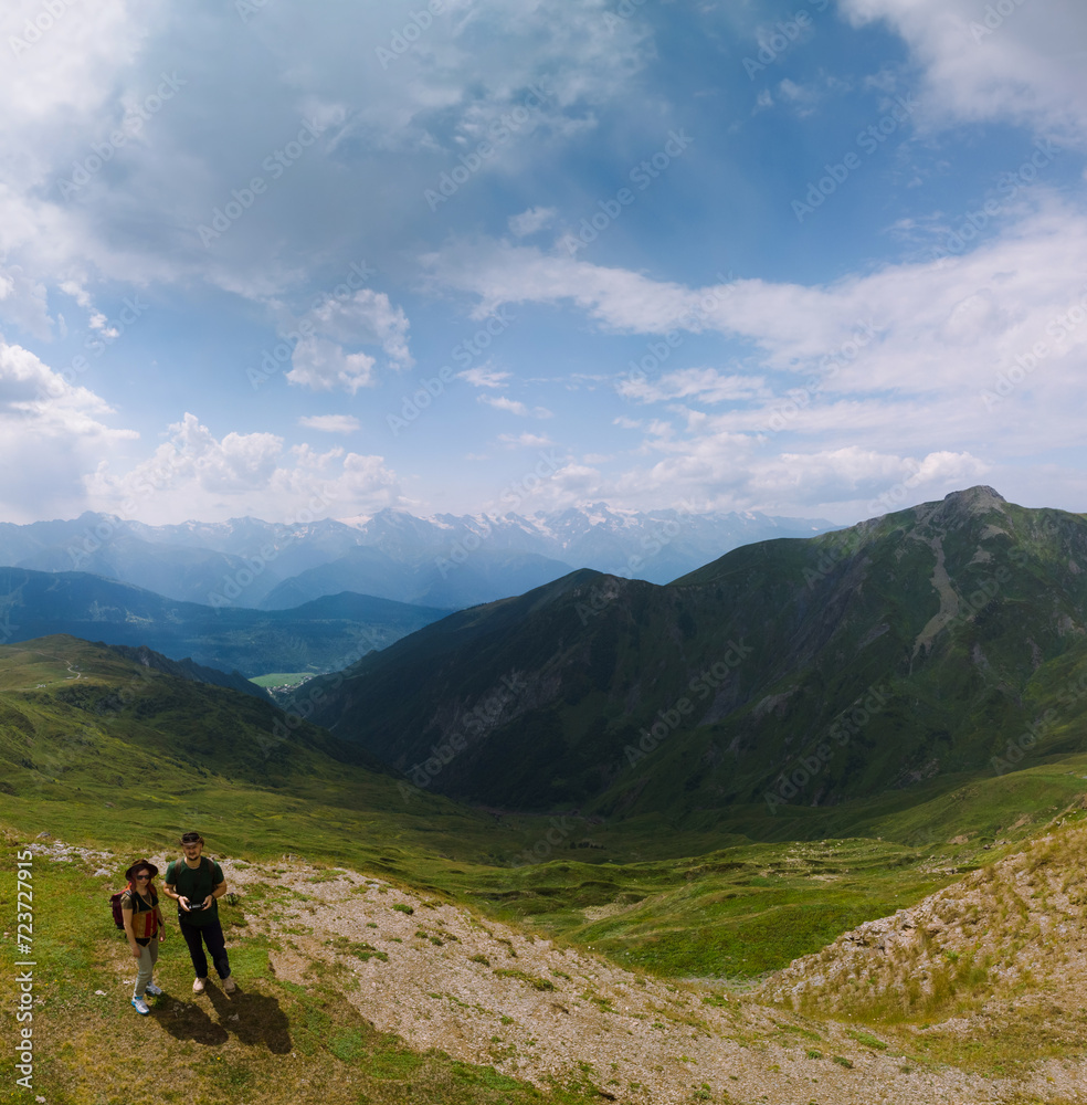 Couple woman and man wearing wide sun hat and backpack, tourists on hiking trail to Koruldi Lakes, Svaneti region, Mestia Georgia. The concept of travel and active recreation. Summer day. Aerial