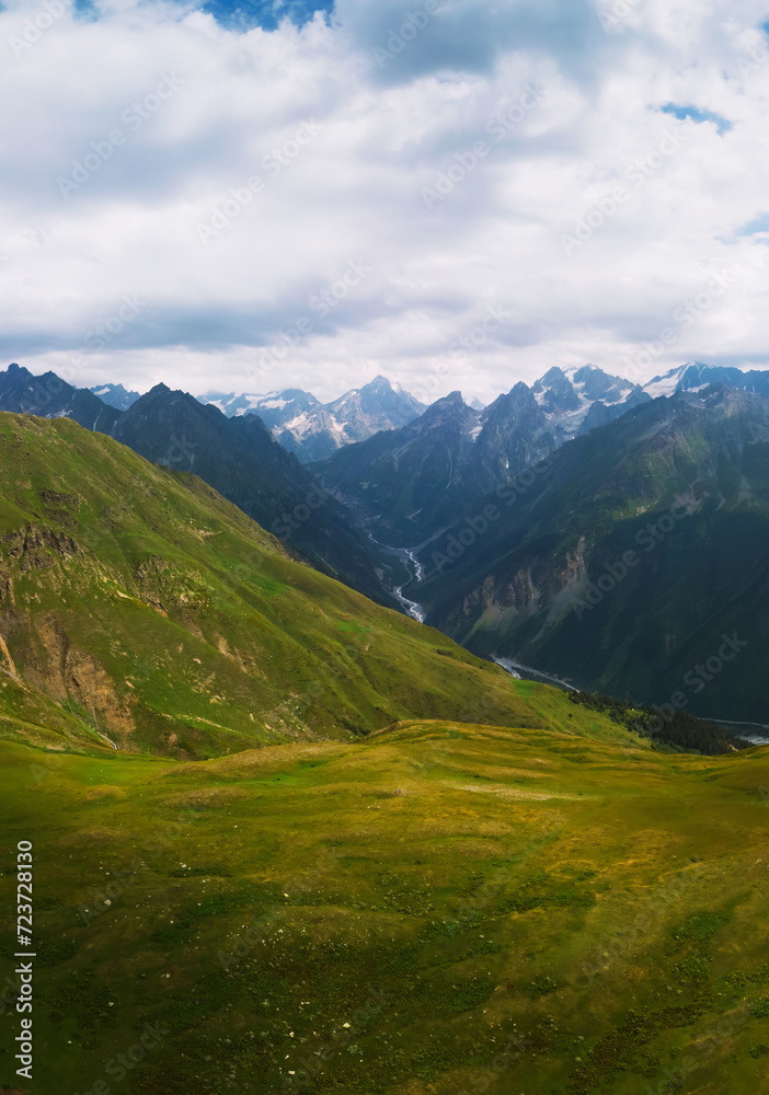 Aerial view at the Koruldi lakes. Green hills, high mountain pastures. Summer day. in the background are the snowy peaks of the Caucasus Mountains. The concept of hiking. Vertical photo