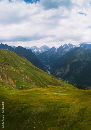 Aerial view at the Koruldi lakes. Green hills, high mountain pastures. Summer day. in the background are the snowy peaks of the Caucasus Mountains. The concept of hiking. Vertical photo