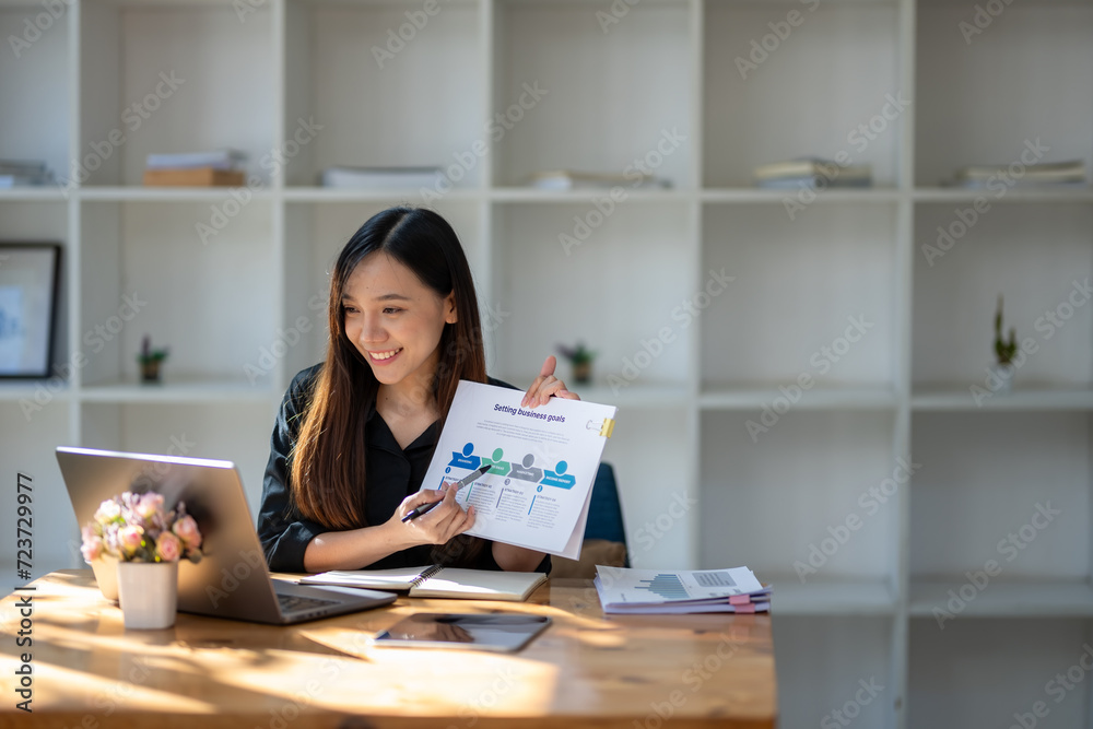 Smiling businesswoman looking at laptop screen and showing data clipboard holding in her hand. Video conference Smiling businesswoman looking at laptop screen and showing data clipboard holding in her hand. Video conference