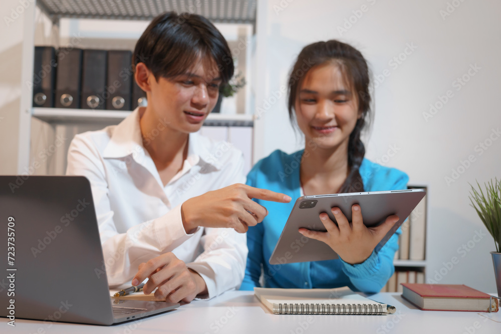 An Asian male consultant and an African American female intern sit at a table with laptops doing paperwork together to discuss a project's financial reports. Company business collaboration concept An Asian male consultant and an African American female intern sit at a table with laptops doing paperwork together to discuss a project's financial reports. Company business collaboration concept