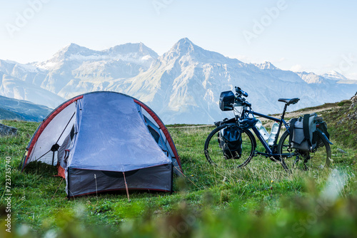 Setting up camp during bike travel in the Alps with tent and a packed bike in the foreground and a high mountain range in the background
