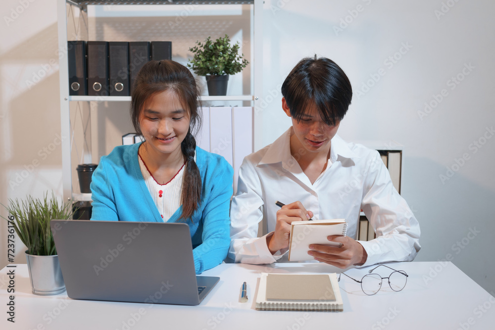 An Asian male consultant and an African American female intern sit at a table with laptops doing paperwork together to discuss a project's financial reports. Company business collaboration concept An Asian male consultant and an African American female intern sit at a table with laptops doing paperwork together to discuss a project's financial reports. Company business collaboration concept