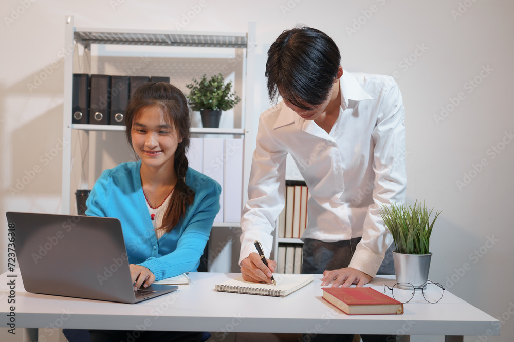 An Asian male consultant and an African American female intern sit at a table with laptops doing paperwork together to discuss a project's financial reports. Company business collaboration concept An Asian male consultant and an African American female intern sit at a table with laptops doing paperwork together to discuss a project's financial reports. Company business collaboration concept