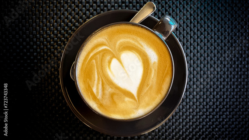 Delicious golden flat white Timorese coffee with love heart shape in modern black cup and saucer, top down birds eye view photo