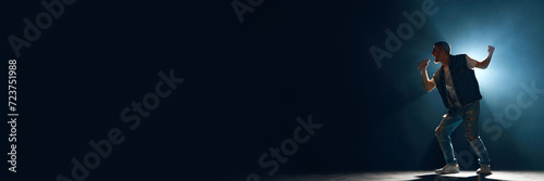 Banner. Man, artist singing with microphone in smoke illuminated blue stage light against dark background with negative space for text. Concept f music and dance, lifestyle, festivals, concerts. Ad