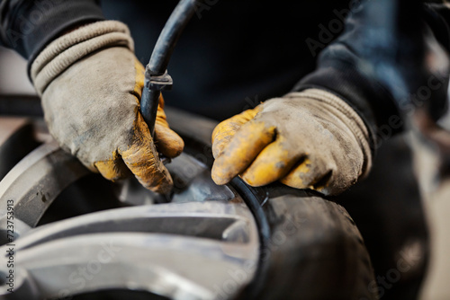 Close up of hands holding a hose and pumping a car tire at vulcanizing workshop. © dusanpetkovic1