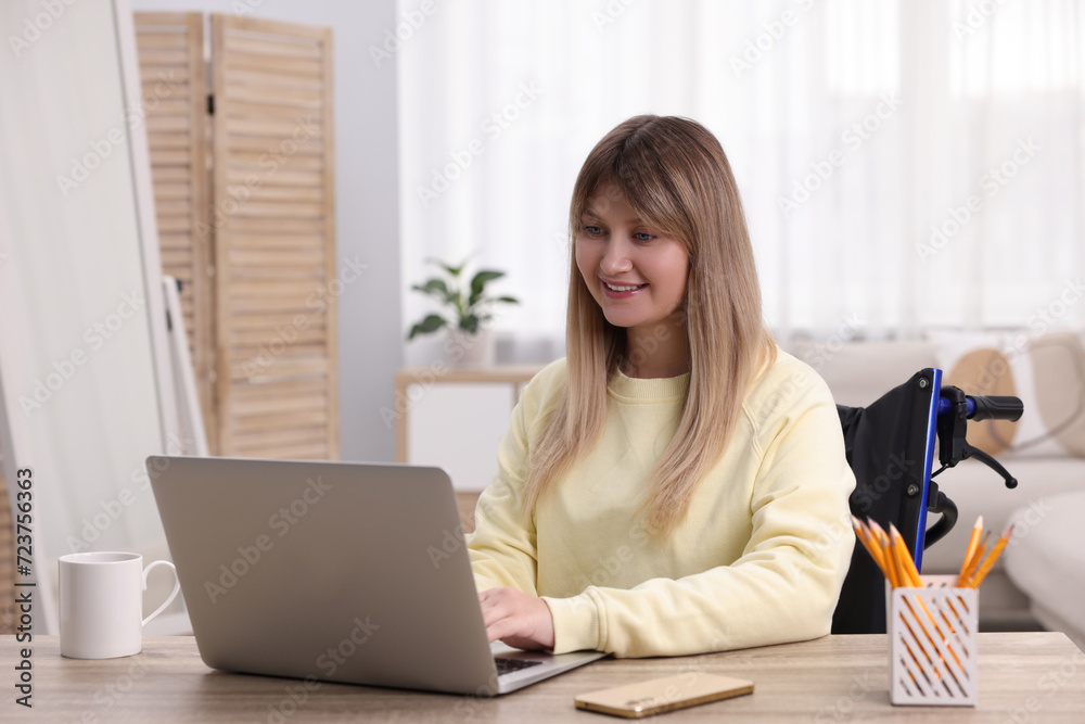 Woman in wheelchair using laptop at table in home office Woman in wheelchair using laptop at table in home office