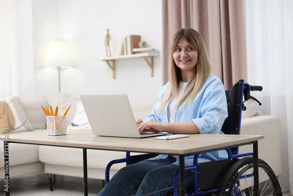Woman in wheelchair using laptop at table in home office Woman in wheelchair using laptop at table in home office