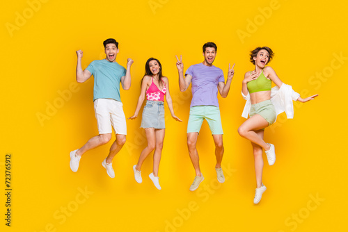Full length photo of excited people jumping enjoy discount make v sign raise hands up isolated shine color background