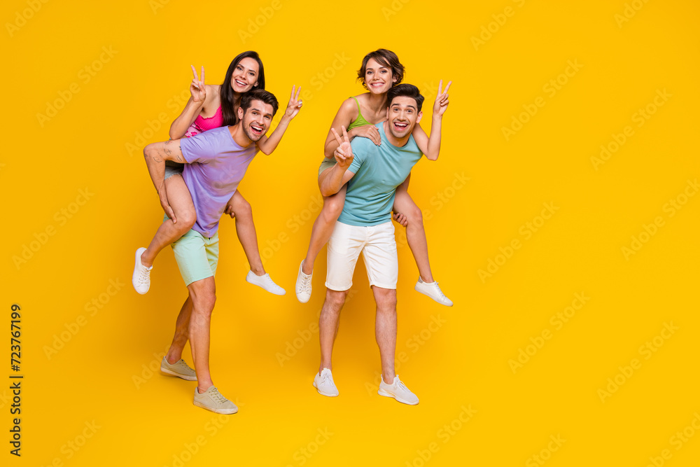 Full length photo of positive cheerful people have fun together girls make v sign guys piggyback isolated bright color background