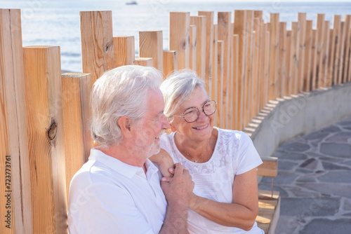 Cheerful senior couple smiles carefreely while sitting outdoors in the sunset light, two cheerful pensioners together by the sea expressing freedom and serenity photo