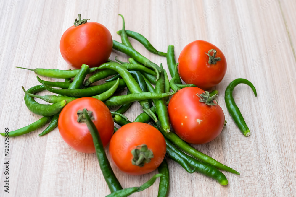 Red tomato and green chili pepper on plain wooden table, green essential vegetables for all essential foods, view of unpeeled vegetables with plain background