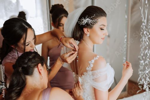 Wedding morning. Bridesmaids help put on the white wedding dress. A young woman is preparing to meet her groom and having fun with her friends photo