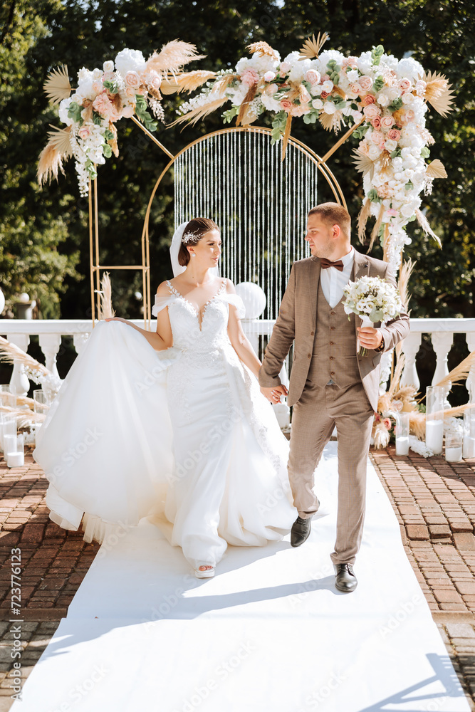 the bride and groom are walking against the background of the wedding arch. Outdoor wedding ceremony. Groom and bride on the background of the wedding arch.
