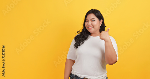 A chubby Asian woman wearing a white t-shirt makes a gesture of agreement and satisfaction with something on a yellow background.