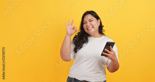 A chubby Asian woman wearing a white t-shirt was excited and happy when she saw a message on her phone on a yellow background