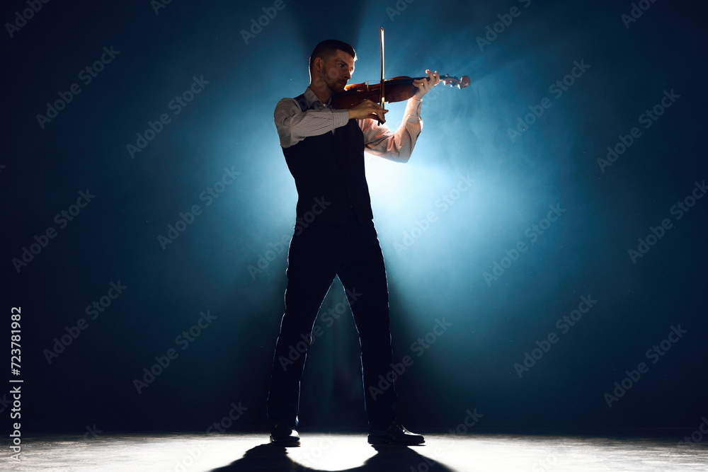 Lost in melody. Violinist in formal wear playing with passion on stage with dramatic smoke lit by backlight. Concept of instrumental music festivals and concerts, art, culture. Ad Lost in melody. Violinist in formal wear playing with passion on stage with dramatic smoke lit by backlight. Concept of instrumental music festivals and concerts, art, culture. Ad