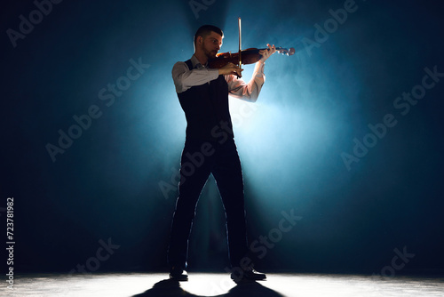Lost in melody. Violinist in formal wear playing with passion on stage with dramatic smoke lit by backlight. Concept of instrumental music festivals and concerts, art, culture. Ad