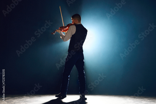Professional musician with violin under performing his new melody on stage with spotlights showcasing classical music's allure. Concept of instrumental music festivals and concerts, art, culture. Ad