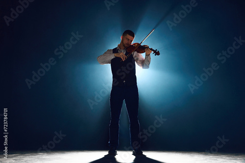 Intense violin recital with musician standing on stage with backlights against darkness with smoke. Concept of instrumental classic music festivals and concerts, art, culture. Ad photo