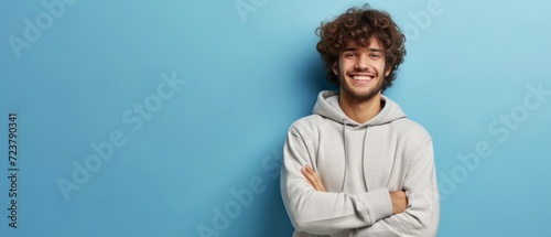 Portrait of happy man with curly hair smile toothily keeps arms down wears casual hoodie looks cheerful isolated over blue background being in good mood with copy space. Generative ai photo