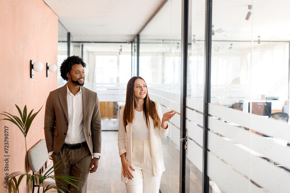 Obraz premium African-American businessman and his female colleague share a strategy vision walking through the office, with genuine smiles indicating a positive work culture. Concept of collaboration and teamwork