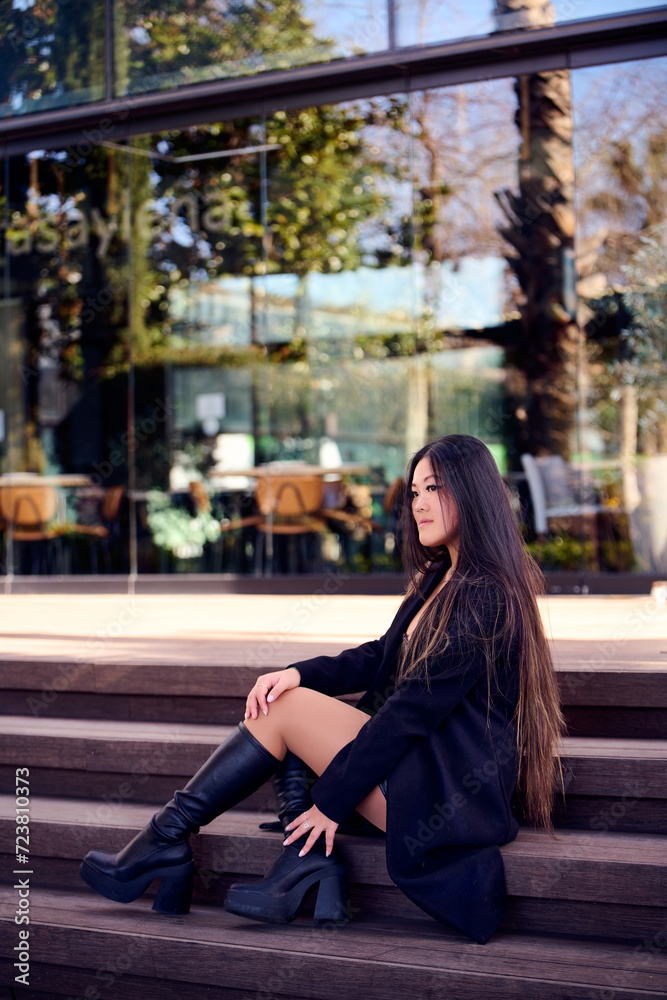 Fototapeta premium Portrait of a beautiful young Asian woman in a black coat and boots