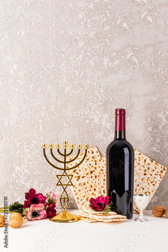 Vertical festive background for Jewish Passover holiday with traditional matzoth bread, red wine, flowers and golden minor candlestick. A copy space.