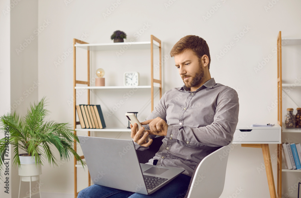 Business man using mobile phone and laptop. Young man sitting on chair with notebook computer at home, holding his cellphone, reading news on social media app, dialing number, or typing text message Business man using mobile phone and laptop. Young man sitting on chair with notebook computer at home, holding his cellphone, reading news on social media app, dialing number, or typing text message