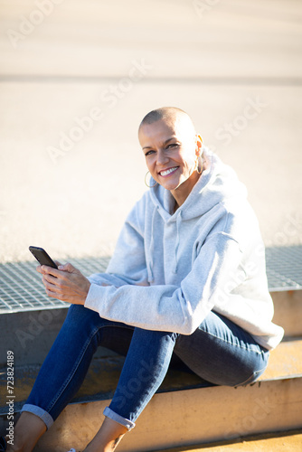 smiling woman with shaved head holding cellphone